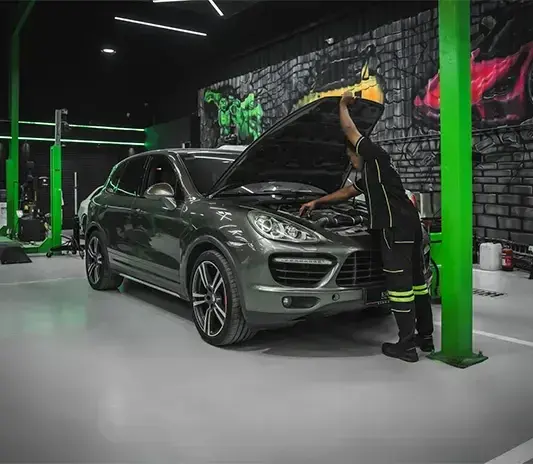Technician working under the open bonnet of a Porsche Cayenne in the Mussafah workshop
