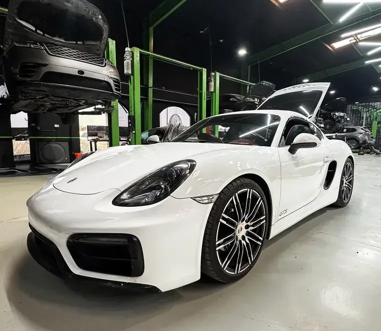 White Porsche Cayman GTS between the green lifts of the Mussafah workshop